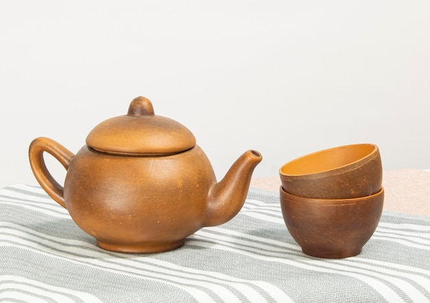 Tetera marrón de cerámica con tazas sobre un fondo de mesa blanco