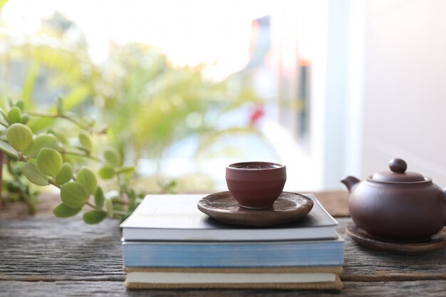 Tetera marrón y taza de té y libros sobre mesa de madera