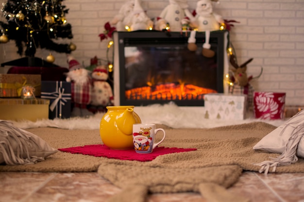 Tetera y taza de café caliente, en la alfombra rodeada de adornos navideños y luces.