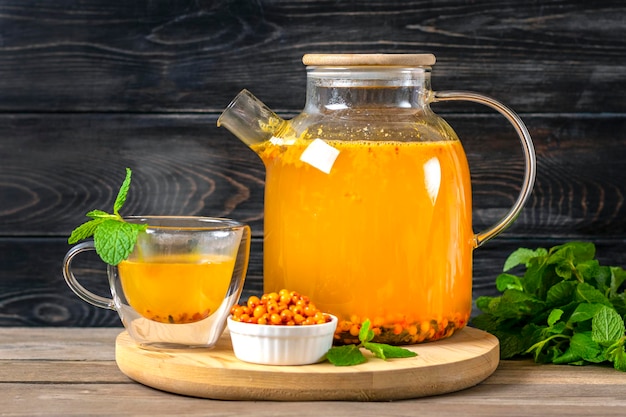 Tetera y taza de té de espino amarillo con menta y miel en la mesa de madera