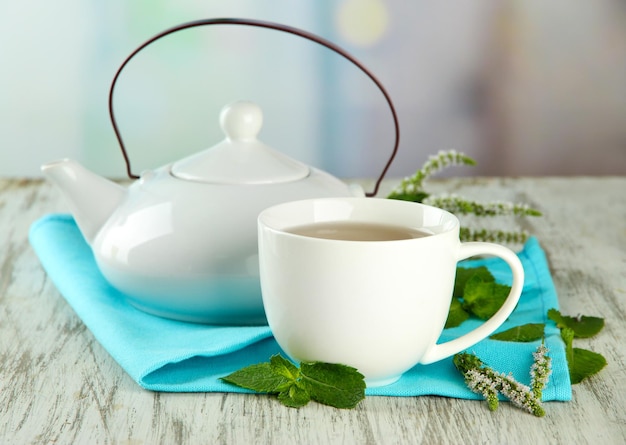 Tetera y taza de té de hierbas con flores de menta fresca en la mesa de madera