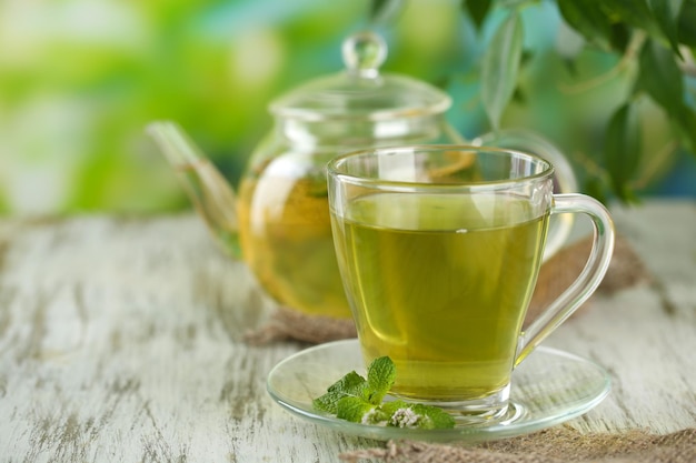 Tetera y taza de té de hierbas con flores de menta fresca en la mesa de madera