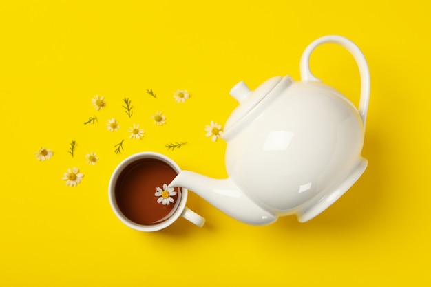 Tetera y taza de té de manzanilla sobre fondo amarillo, vista superior