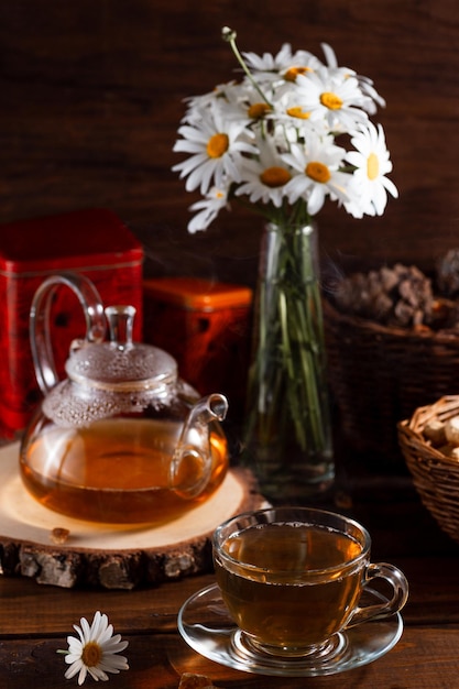 Una tetera y una taza de té sobre una mesa de madera y un ramo de margaritas