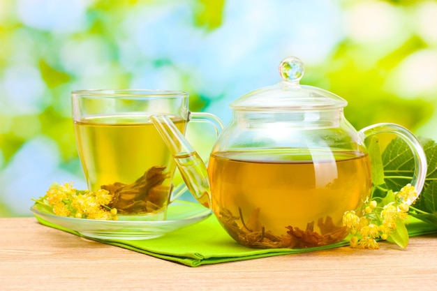 Tetera y taza con té de tilo y flores sobre la mesa de madera en el jardín