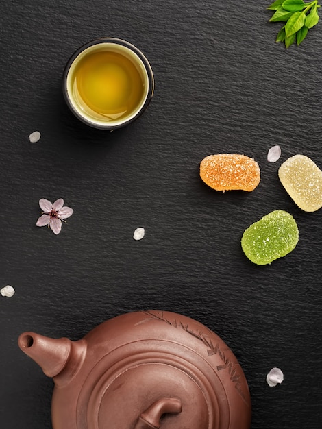 La tetera y las tazas pequeñas con té verde se encuentran en una mesa de piedra negra junto a los dulces.