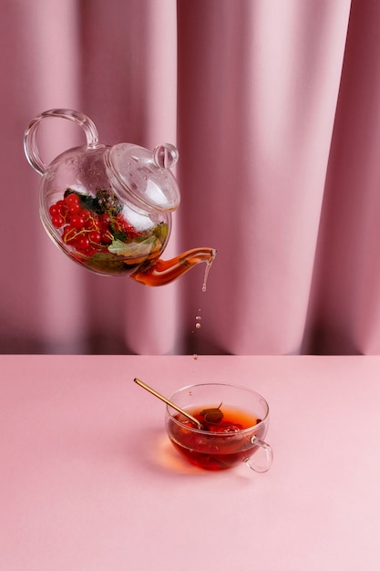 Tetera con té de bayas levitando sobre la taza