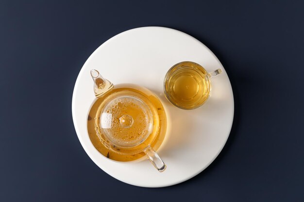 Tetera con té de hierbas verdes con vaso de vidrio en podio blanco sobre fondo azul Té caliente Vista superior