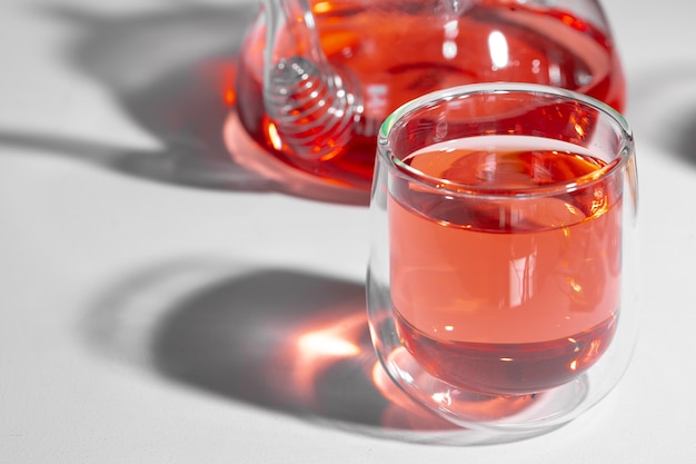 Tetera de vidrio y taza de vidrio con té sobre fondo blanco con largas sombras de cerca