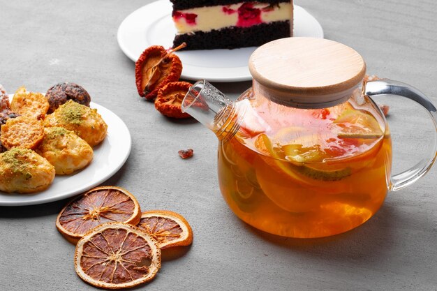 Tetera de vidrio con té de frutas y galletas sobre fondo gris