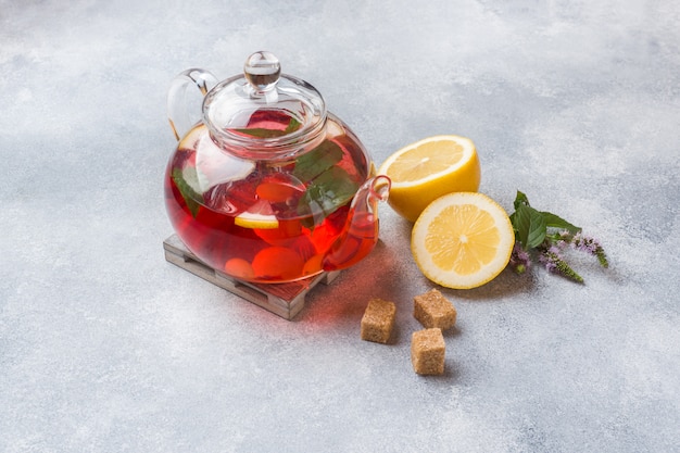 Tetera de vidrio con té, menta y limón en mesa gris con espacio de copia.