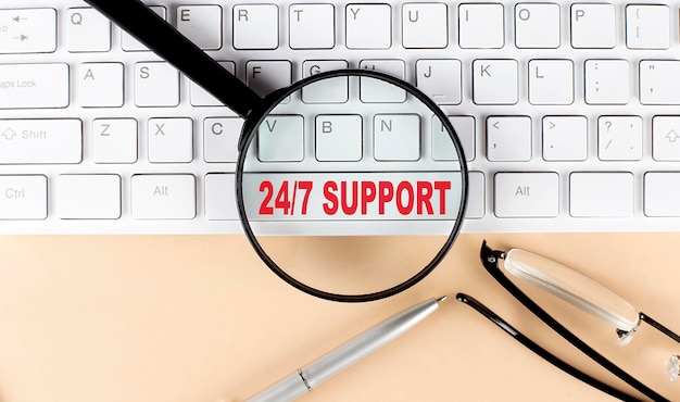 Text 24 7 SUPPORT auf Tastatur mit Lupenbrille und Stift auf beigem Hintergrund