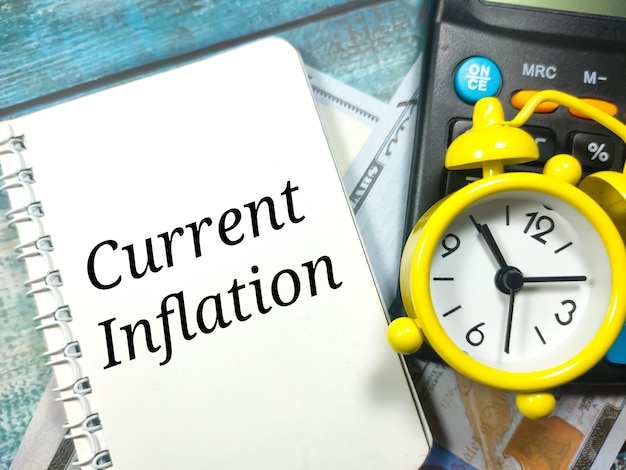 Text aktuelle Inflation auf Notizbuch mit Uhrenrechner und Banknoten geschrieben