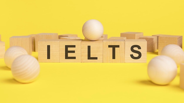 Text IELTS auf Holzwürfeln hellgelbe Oberfläche Holzkugelkugeln unter den Holzwürfeln unterschiedlich und Position im Nischenmarktkonzept IELTS International English Language Testing System