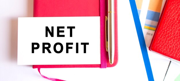 Text NET PROFIT auf weißer Karte auf Notizblock liegend. Finanzkonzept.