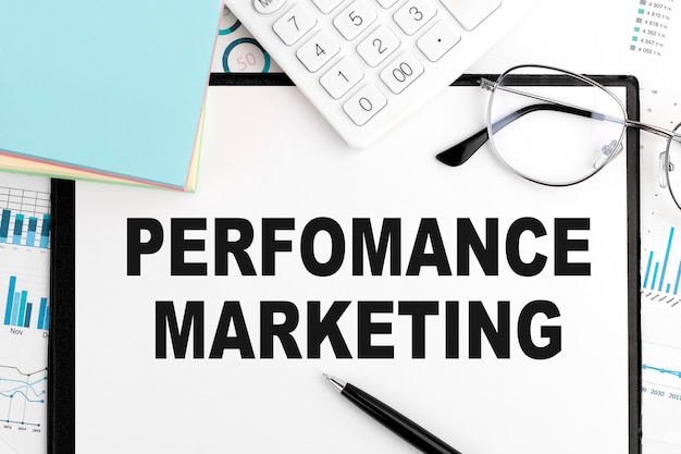 Text Performance Marketing auf Zwischenablage, Stift, Brille, Taschenrechner, Aufkleber, Grafiken. Geschäftskonzept. Flach liegen.