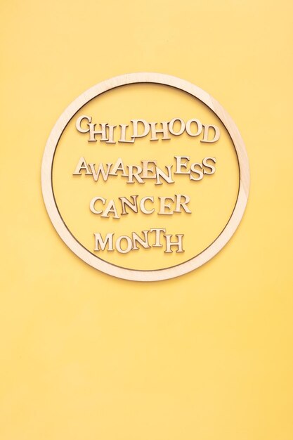 Text zum Monat des Bewusstseins für Krebs im Kindesalter aus Holzbuchstaben in rundem Holzrahmen auf gelbem Hintergrund Hochformat