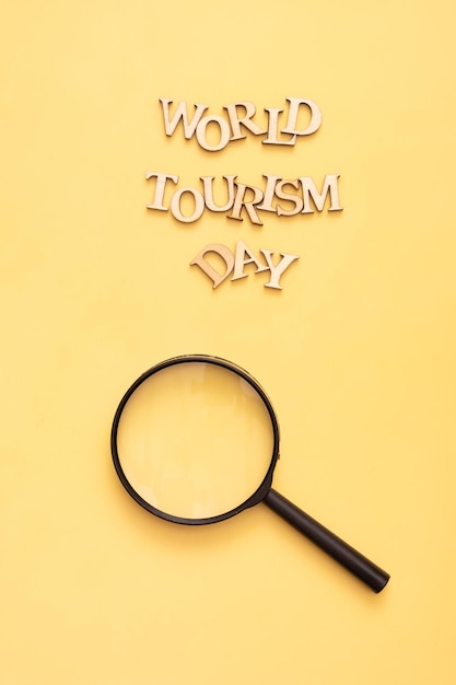 Text zum Welttourismustag aus Holzbuchstaben auf gelbem Hintergrund mit Lupe