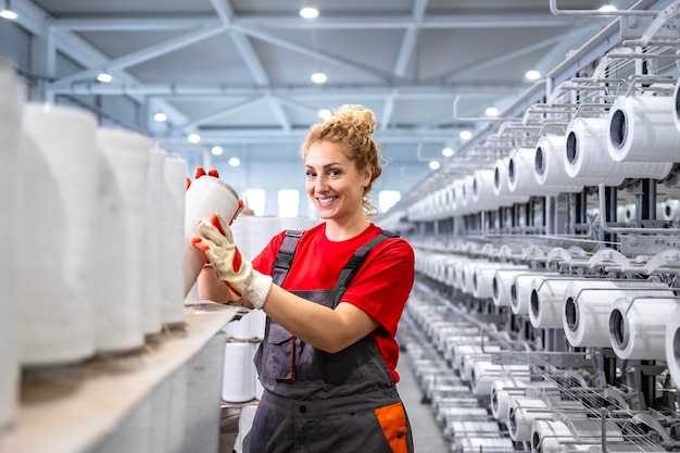 Textilfabrikarbeiterin mit Fadenrollen und einer industriellen Nähmaschine im Hintergrund