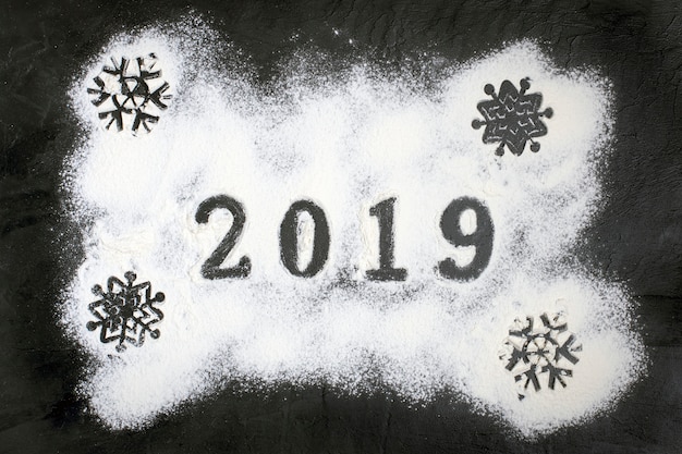 Texto 2019 hecho con harina con decoraciones sobre fondo negro. Feliz navidad h