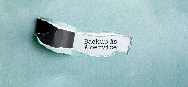 Foto el texto backup as a service que aparece detrás del papel verde rasgado