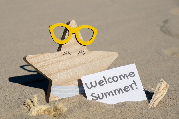 Foto texto de bienvenida al verano en tarjeta de felicitación de papel sobre el fondo de estrellas de mar divertidas en gafas verano