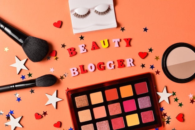 Texto de blogger de belleza sobre un fondo naranja. Productos de maquillaje profesionales de moda con productos cosméticos de belleza, sombras de ojos, pestañas, cepillos y herramientas.