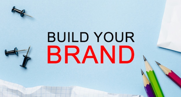 Foto texto build your brand en un bloc de notas blanco con lápices sobre un fondo azul. concepto de negocio