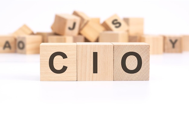 Texto CIO Chief Information Investment Officer está escrito em três cubos de madeira em pé sobre uma mesa branca ao fundo uma montanha de cubos de madeira com letras