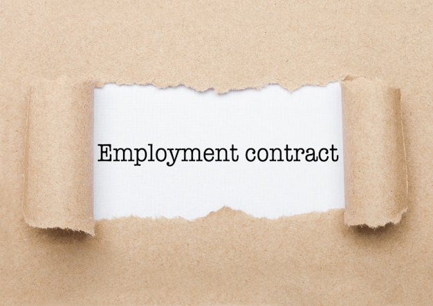 Texto de concepto de contrato de trabajo que aparece detrás de un sobre de papel marrón rasgado
