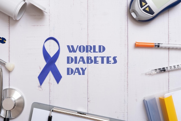 Texto del Día Mundial de la Diabetes con estetoscopio de glucómetro y jeringas con una tableta en una vista superior de fondo de madera