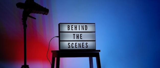 Texto dos bastidores em Lightbox ou Cinema Light box. Caixa de luz de placa de filme na escada do estúdio e tripé de luz Snoot em cores de fundo gradiente. Representar nos bastidores a equipe está trabalhando.