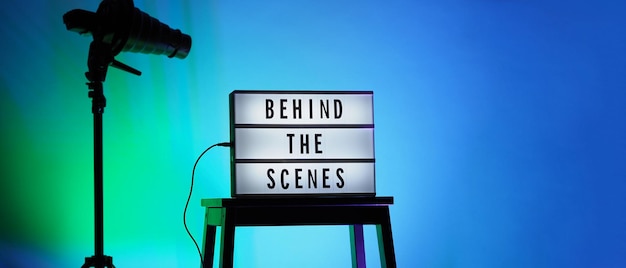 Texto dos bastidores em Lightbox ou Cinema Light box. Caixa de luz de placa de filme na escada do estúdio e tripé de luz Snoot em cores de fundo gradiente. Representar nos bastidores a equipe está trabalhando.