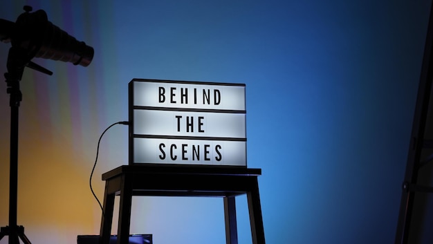 Texto dos bastidores em Lightbox ou Cinema Light box. Caixa de luz de placa de filme na escada do estúdio e tripé de luz Snoot em cores de fundo gradiente. Representar nos bastidores a equipe está trabalhando.