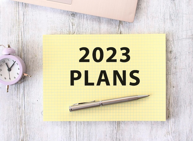 Foto texto dos planos 2023 escrito em um caderno sobre uma mesa de trabalho de madeira ao lado de um laptop