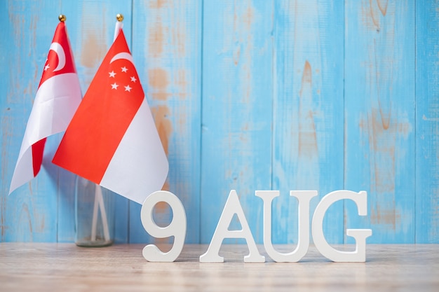 Texto em madeira de 9 de agosto com bandeiras em miniatura de Cingapura. Dia da independência de Cingapura, dia nacional da cidade-estado e conceitos de república feliz