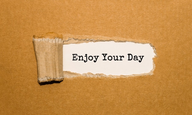 El texto Enjoy Your Day que aparece detrás de un papel marrón rasgado