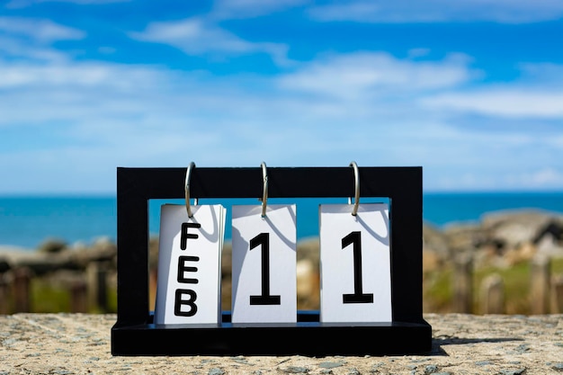 Foto texto de la fecha del calendario del 11 de febrero en marco de madera con fondo borroso del concepto de fecha del calendario oceánico