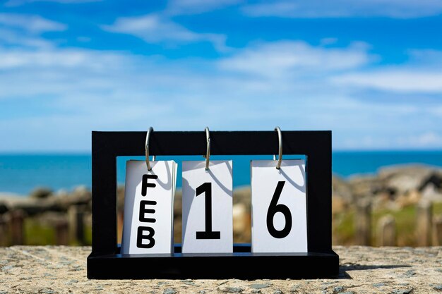 Foto texto de la fecha del calendario del 16 de febrero en marco de madera con fondo borroso del concepto de fecha del calendario oceánico