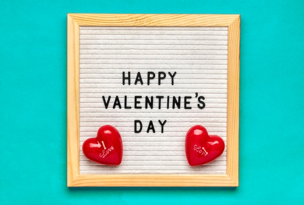 Texto Feliz día de San Valentín en tablero de fieltro velas rojas en forma de corazón sobre fondo azul