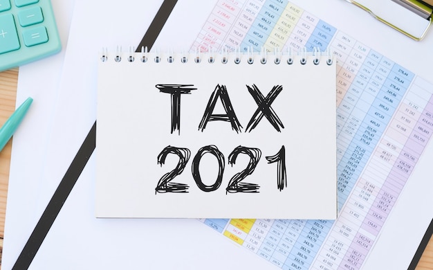 Texto imposto 2021 no bloco de notas com calculadora, clipes e caneta no relatório financeiro. foto do conceito financeiro e de negócios