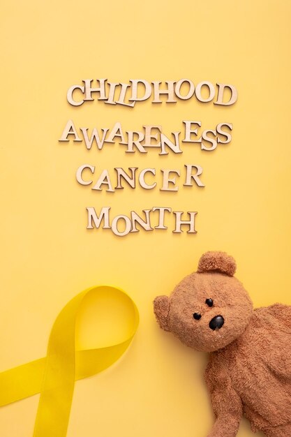 Texto del mes de concientización sobre el cáncer infantil con cinta y oso de peluche sobre fondo amarillo Formato vertical