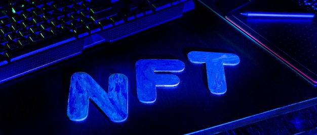 Texto NFT Non-Fungible Token de letras iluminadas com luz de néon azul. Local de trabalho de um designer gráfico criando arte digital NFT. Conceito de criptoarte