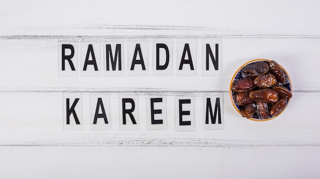 Foto texto de ramadán kareem con un tazón de fechas jugosas en el escritorio blanco