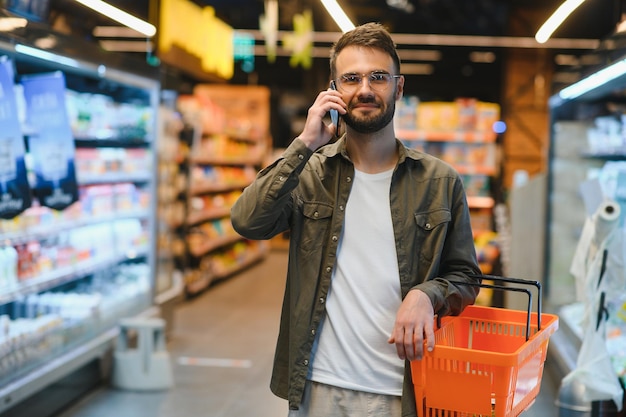 Texto rápido durante as compras Jovem bonito segurando celular e sorrindo enquanto está de pé em uma loja de alimentos