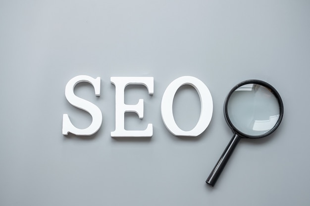 Texto de SEO (Search Engine Optimization) y lupa en gris. Concepto de idea, visión, estrategia, análisis, palabra clave y contenido