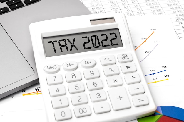 Texto TAX 2022. Vista superior de la máquina de calcular, computadora portátil y cuadros, documentos y gráficos. Concepto de impuestos y negocios sobre fondo blanco.