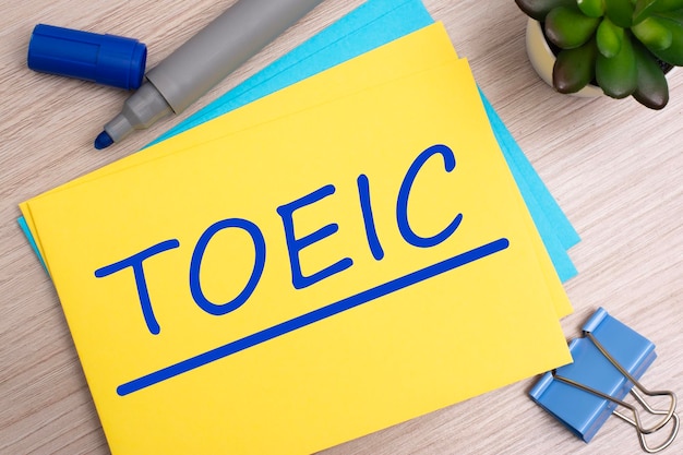 Texto toeic en papel amarillo sobre fondo de madera clara con papelería