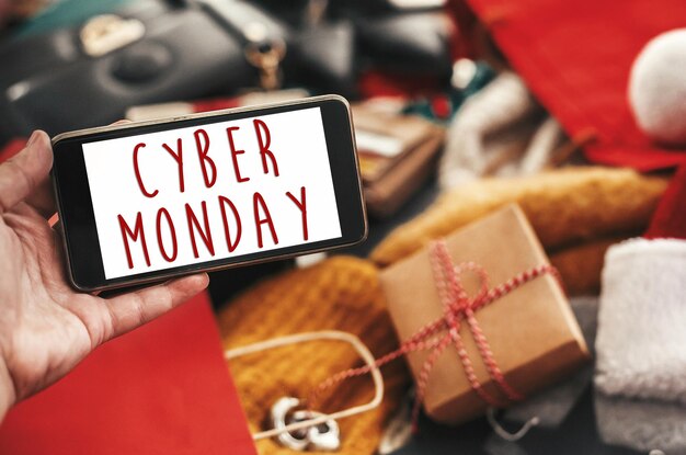 Texto de venta de Cyber Monday en la pantalla del teléfono Signo de venta de Navidad Descuento especial Signo de oferta de Navidad Teléfono de mano con mensaje publicitario en tarjetas de crédito bolsas ropa regalos