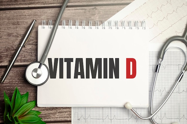 Texto VITAMIN D en un cuaderno con estetoscopio y bolígrafo sobre fondo de madera